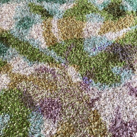 Close-up detail of yarn ends of the thick pile in various colours. The texture is pixelated and the woven shapes created by different colours have blurry edges.