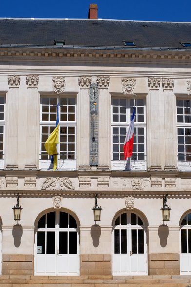 Facade de l'Hôtel de ville richement décorée, en tuffeau et toiture en ardoise. Ciel totalement bleu. Deux drapeaux, Ukrainien en berne a priori, et français. Au milieu, à l'étage, la grande méridienne en ardoise et ferronnerie marque quasiment midi solaire avec son œilleton en forme de disque solaire doré, percé en son centre.