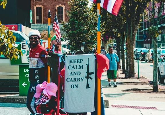 A photograph of a street in the US with a banner saying 'Keep calm and carry on' with an image of a semi-automatic rifle next to it.