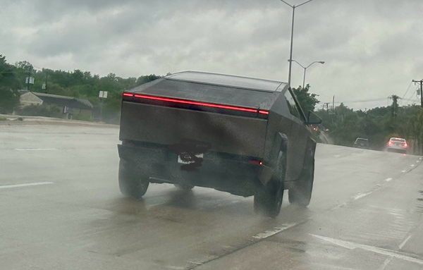Photo from behind a Tesla Cybertruck on a rainy day, driving down the road.