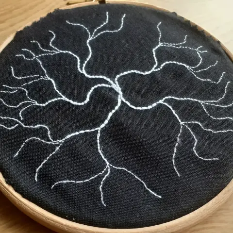 Small embroidery ring containing dark material with white thread branching out from the center of the ring.