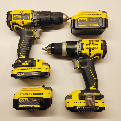 On the left side of the square layout, there's a Stanley FatMax screw gun with an additional battery positioned underneath it. On the right side, there's a battery with the screw gun placed horizontally and facing in the opposite direction directly above it. The tools and batteries complement each other in shape of a square, with the chuck of the screw gun on the right aligning with the handle of the screw gun on the left. The dimensions of the batteries complement the length and height of the screw guns.
