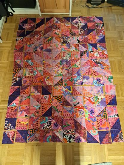 Quilt mit einem Design aus Half Square Triangles in Lila und Pink Tönen.