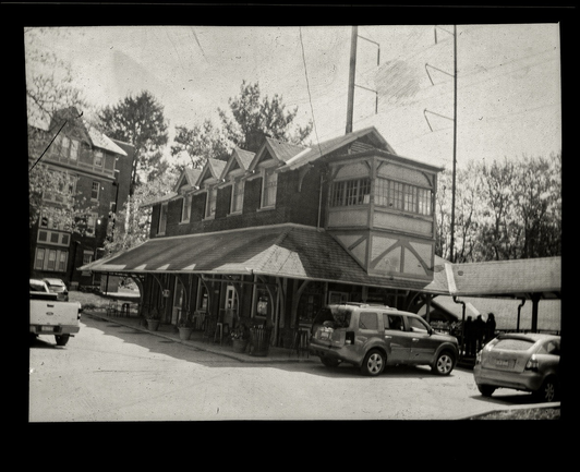 Black and white photo of an old train station building with cars parked around it.