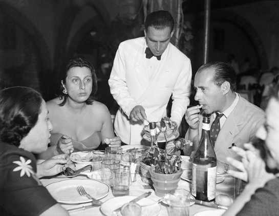 Magnani looking beat, finishing her meal, while Rossellini listens intensely to one of the other guests at the table. All the while a waiter serves the next course.