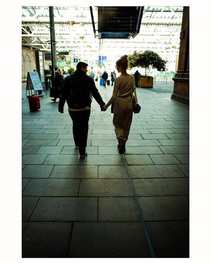 A young couple holding hands, largely in silhouette, as they head to catch a train.