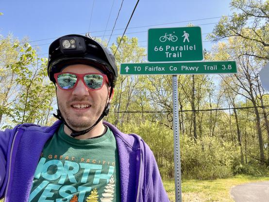 Selfie in front of green bike trail signs reading “66 Parallel Trail” and “TO Fairfax Co Pkwy Trail 3.8”
