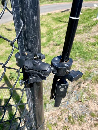 A double clamp with ball sockets holds onto a chain link fence and a selfie stick