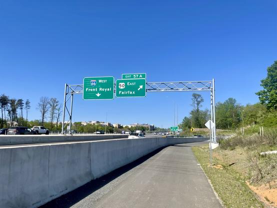 A paved trail is separated by a concrete wall next to a freeway with signs for 66 West to Front Royal and US-50 East to Fairfax