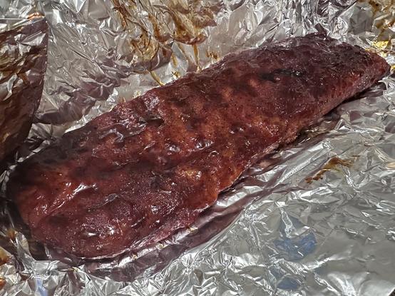 A cooked rack of ribs on aluminum foil.
