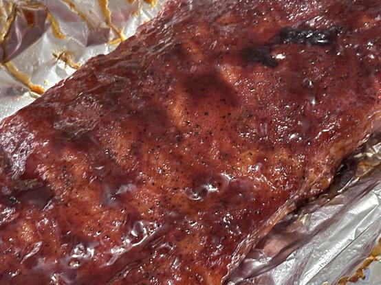 A rack of barbecued ribs on aluminum foil.