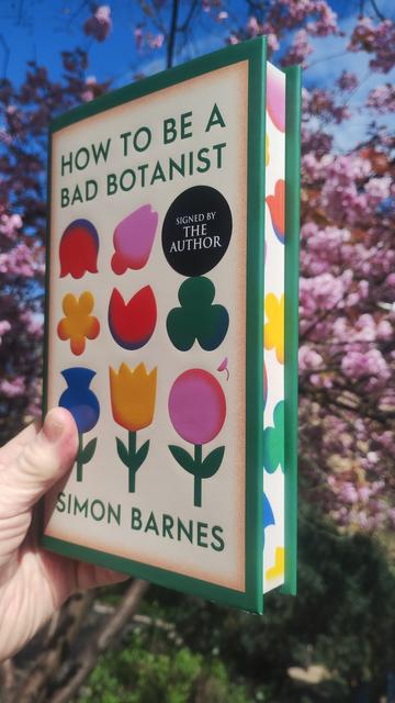 A copy of How to be a Bad Botanist, with colourful flower illustrations on the cover, and more on the spredges (sprayed edges of the pages), and green border around it all, with bright, pink cherry blossoms behind it.