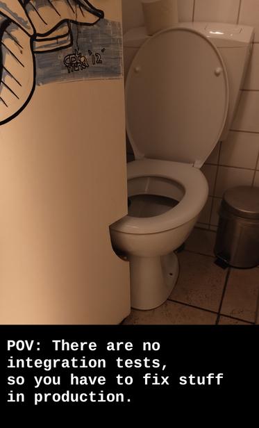 Picture shows a very narrow toilet room. The toilet is open, a roll of toilet paper standing on the water tank. 
The door is half way open. It has a cutout at the lower part of the door to allow it to swing open beyond the toilet, that would otherwise block the door.
Some white text on a black background  in the lower quarter of the picture reads "POV: There are no integrations tests, so you have to fix stuff in production."
