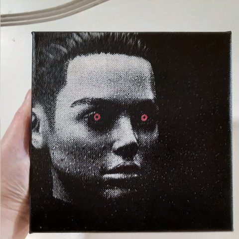 Description by ChatGPT:
The image displays a black canvas held in someone's hand, with a textured portrait created through a pointillist effect. This style uses tiny, distinct dots of a single color applied in patterns to form an image. The portrait features the face of a person looking directly forward. Notably, the individual has striking red eyes, which stand out against the monochromatic black and white of the image. The person's hair is styled short, and the details of their face, including the eyes, nose, and mouth, are crafted from the accumulation of small, precise dots. The surrounding area is less detailed, creating a fade into the deep black of the canvas edges, emphasizing the central features of the face. The stark contrast between the subject's eyes and the rest of the portrait gives it a captivating and intense effect.