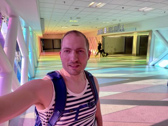 Selfie lit by a purple light in front of a hallway lined with rainbow color windows