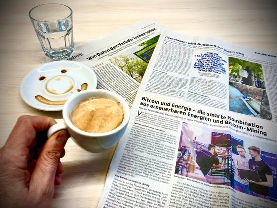 Eine Hand hält eine Kaffeetasse - im Hintergrund sieht man zwei Artikel aus der heutigen Augsburger Allgemeinen zum Thema Smart City in Augsburg.