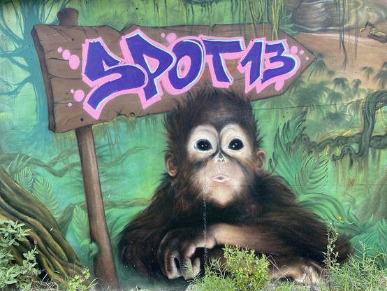 Fresque murale représentant un jeune chimpanzé sur fond de végétation. Au-dessus de sa tête, un panneau indique « SPOT 13 ».