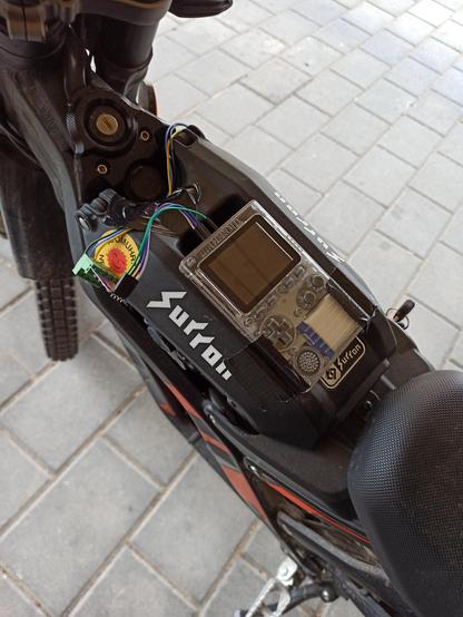 A photo of a gameboy-shaped device attached to the battery cover of a e-moped. There's an RS485 transceiver attached via jumper wires with wires going to the battery.