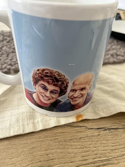 Eine Tasse mit den Bildern zweier lächelnder Menschen, die auf einem Tisch mit einer Stoffserviette stehen.