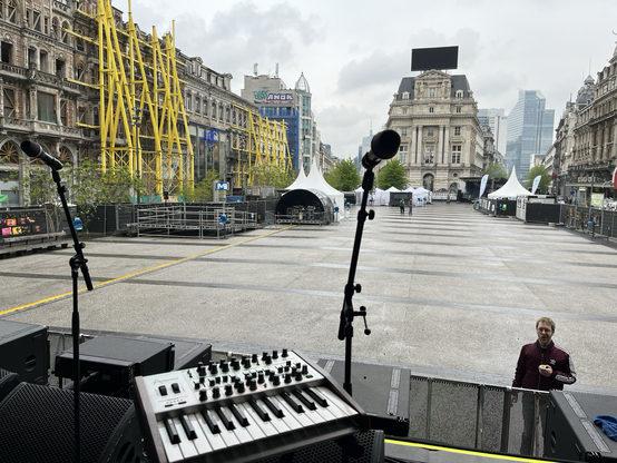 View from a concert stage on a big city square, still without audience, showing a bit of a analogue synth