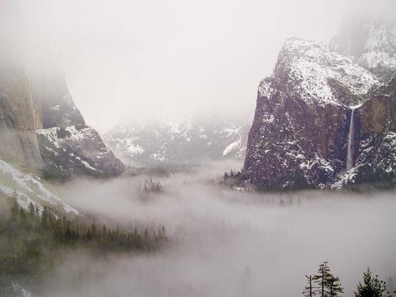 Storm Brewing

This is an image of Yosemite Valley captured from the Tunnel View parking lot. 
The foreground of the image is the floor of Yosemite Valley. The floor is mostly covered in fog with some tree tops rising above it.
To the left is El Capitan. Again most of this iconic rock formation is mostly covered in a cloud with just the middle showing.
To the right is Bridalveil Falls. The waterfall drops into the fog covered valley. 
The background is completely fogged in.