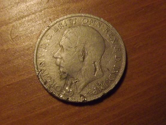 An old coin on a table, showing a head in profile. The text around the edge reads "Georgius V D.C. Britt Omn:Rex F.D. Ind: Imp"