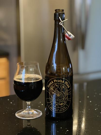 A tall 750ml bottle has yellow lettering with a beehive in a circular frame. The bottle has a wire-hasped stopper rather than a bottle cap. A tulip glass full of beer is to the left.