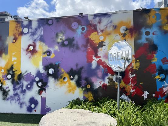 A mirror like stop sign saying “Dream” sits in front of a colorful mural with smoky circles on it