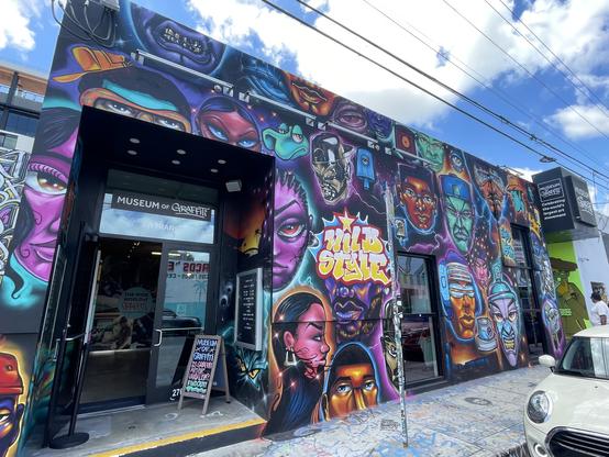Mural of many colorful faces of artists covering the exterior of the Museum of Graffiti