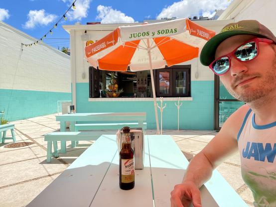 Selfie with my sunglasses on at an aqua blue picnic table outside under a bright white and orange umbrella
