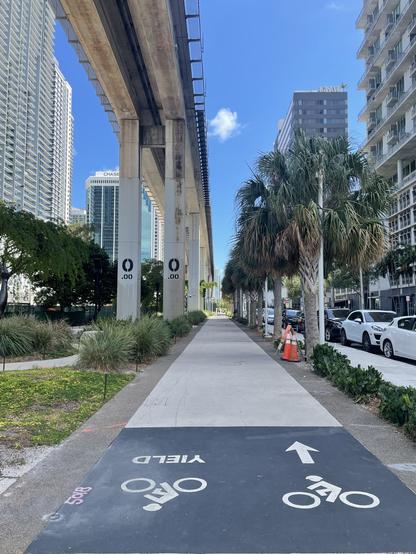 Start of a bike trail underneath elevated tracks with mileage markers reading zero