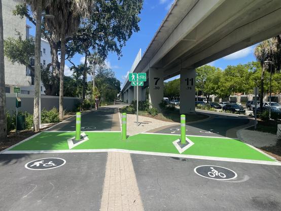 Bright green bollards protect the entrance of a paved trail that splits off between pedestrians and cyclists
