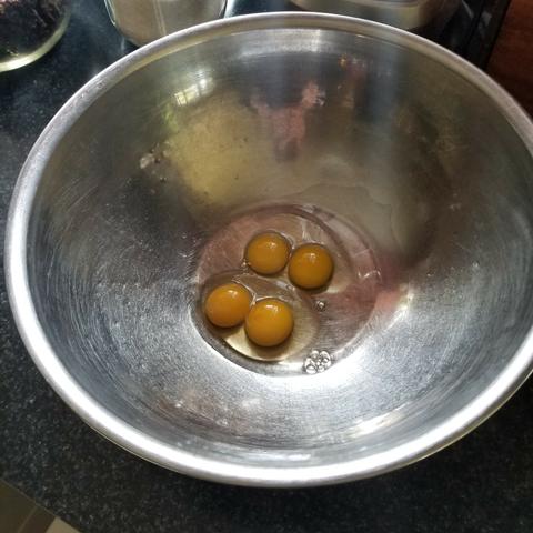 A beat up stainless steel mixing bowl holds 2 double yolk eggs. The eggs are very fresh with firm whites.