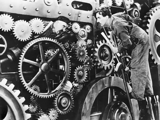 Black/white image with Charlie Chaplin loking into gear wheels, from the movie "Modern Times"