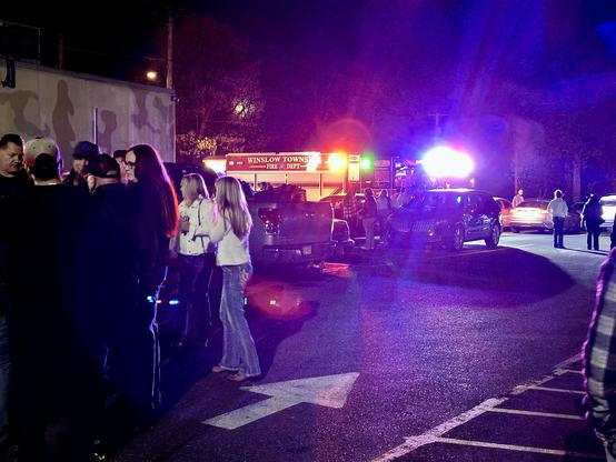 People standing outside The Golden Nugget Tavern in Berlin, NJ after having evacuated the building. A fire truck sits in the background with its emergency lights flashing.