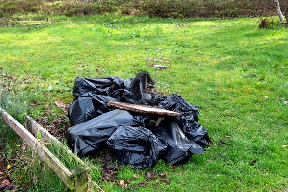 Several bin liners and rubble sacks with a large piece of wood on top.
