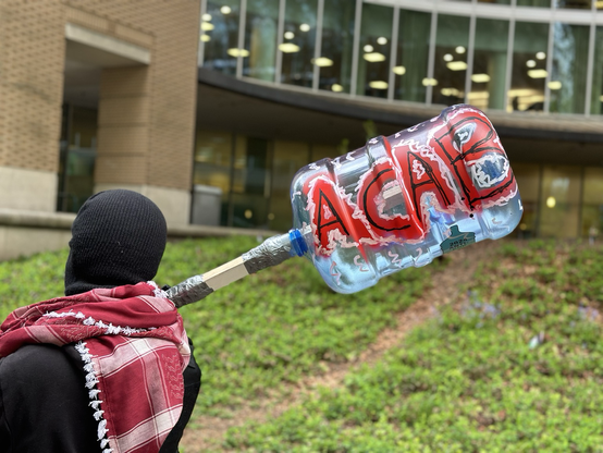 Someone holding a boink bottle connected to a stick and it’s painted with red letters that say “ACAB”