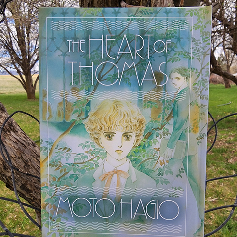 The Heart of Thomas by Moto Hagio, translated by Rachel Thorn, English hardcover a pastel-colored illustration of two boys outside a boarding school among the trees.