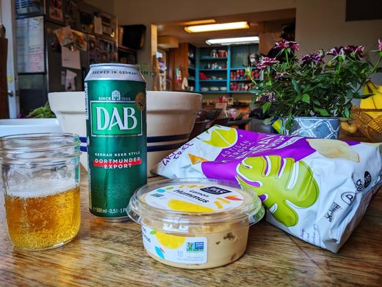 A can of Dortmunder Export beer from the Dortmund brewery DAB, paired with cassava chips and hummus, as seen in the extra-large dining room of my 20-person co-op.