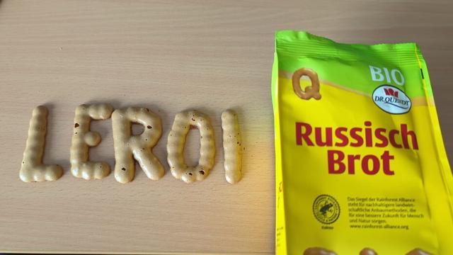 Schriftzug "LEROI" aus "Russisch Brot" sm Tisch aufgelegt, rechts daneben die Verpackung in gelb/grün