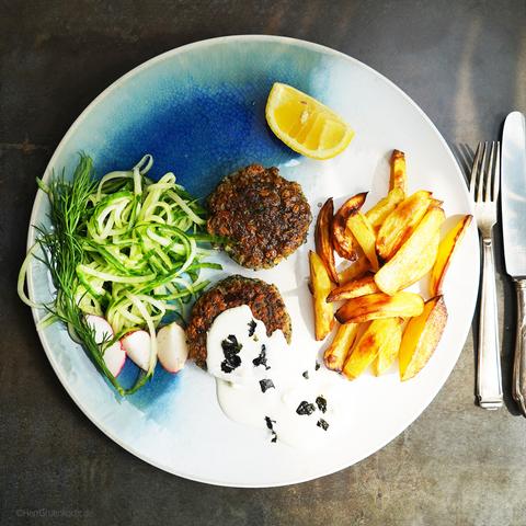 Dunkler Hintergrund. Großer Teller mit Meeresanmutung - also blaue Wellen:-) 2 Frikadellen mit weißer Sauce. Grurkenstreifen und Pommes Frites.