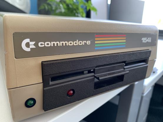 A beige Commodore floppy disk drive, with the Commodore rainbow logo and a dark brown latch mechanism floppy drive.
