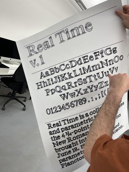 A poster showing type held by a right hand; a left hand pointing on the poster.

The poster reads at the top »Real Time v.1«.
Below it are a character overview and some specimen text.