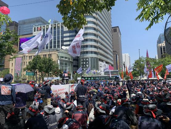 A large crowd holding flags gathers in front of city buildings
