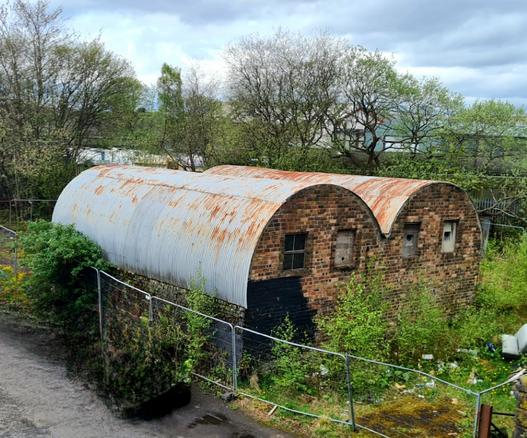 Two huts with brick walls and corrigated iron roofs which seem to have ben made from World War Two Nussen Huts.