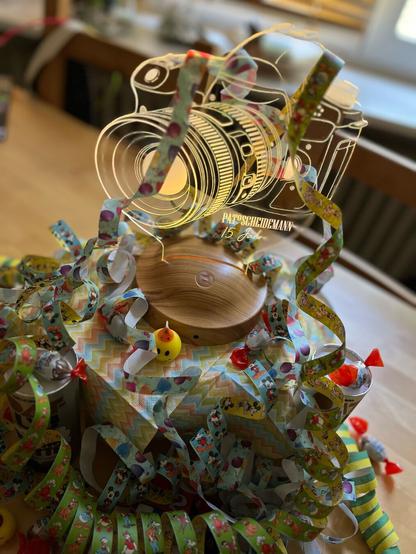 Eine festliche Trophäe mit Luftschlangen und Konfetti auf einem Holzsockel zur Feier des 15-jährigen Jubiläums.

A festive trophy with streamers and confetti on a wooden base, celebrating a 15-year anniversary.