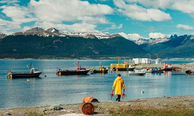 person carrying 2 large red crabs in a small fishing harbor