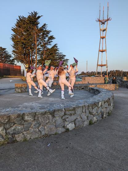Six dancers in white costumes in morning lighting with the Sutro Tower in the background.