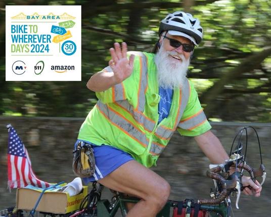 Photo of Bruce Ohlson wearing a reflective yellow vest and white helmet waving from his touring bicycle. The bike has a small American flag on the back. Bruce has a long white beard and is wearing sunglasses. The Bike to Wherever Days 2024 logo is in the upper left-hand corner with sponsor logos for MTC, 511 SF Bay, and Amazon.