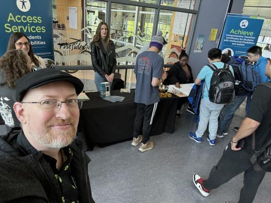Me in front of a table surrounded by college students, behind the table are banners for the Access Services department and Achieve program.